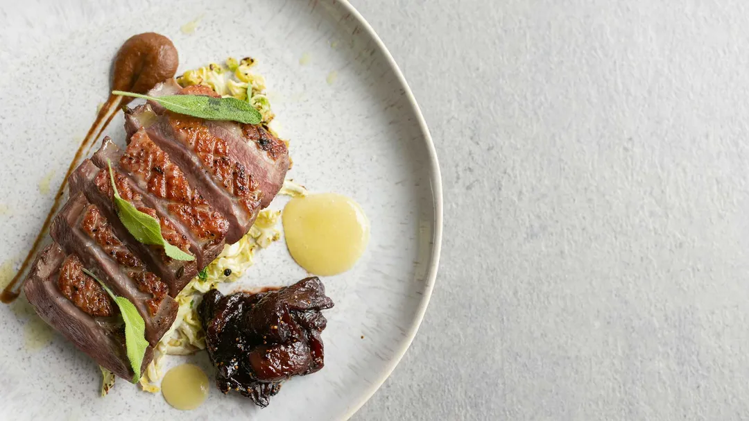 Angerichtetes Fleischgericht mit Salbei, Rotkraut und Sauce auf weißem Teller