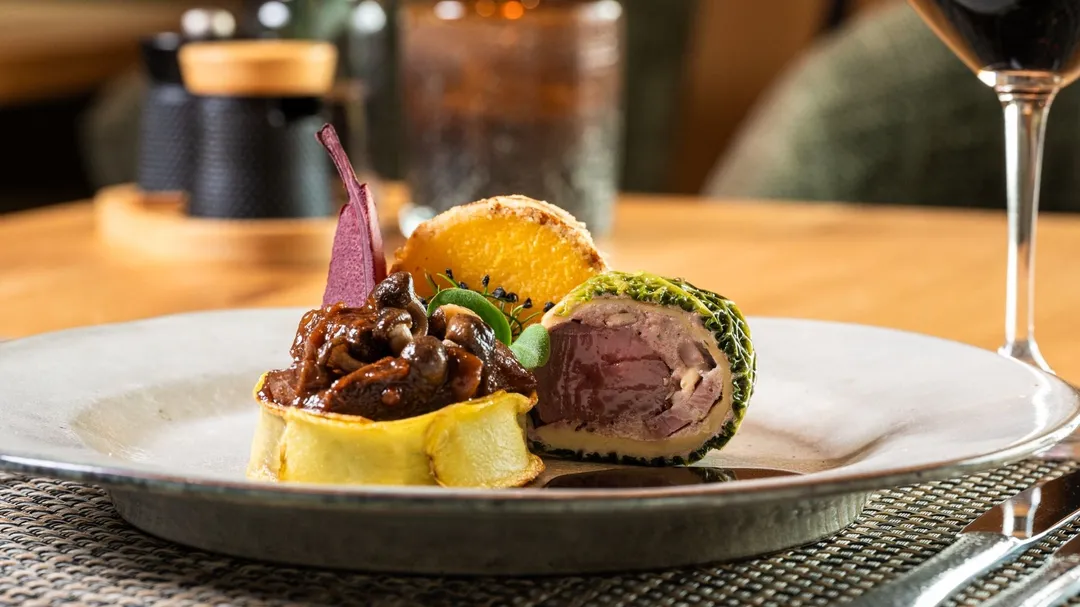 Fleischgericht mit Kräuterkruste, Pilzen und Kartoffelrösti auf Teller