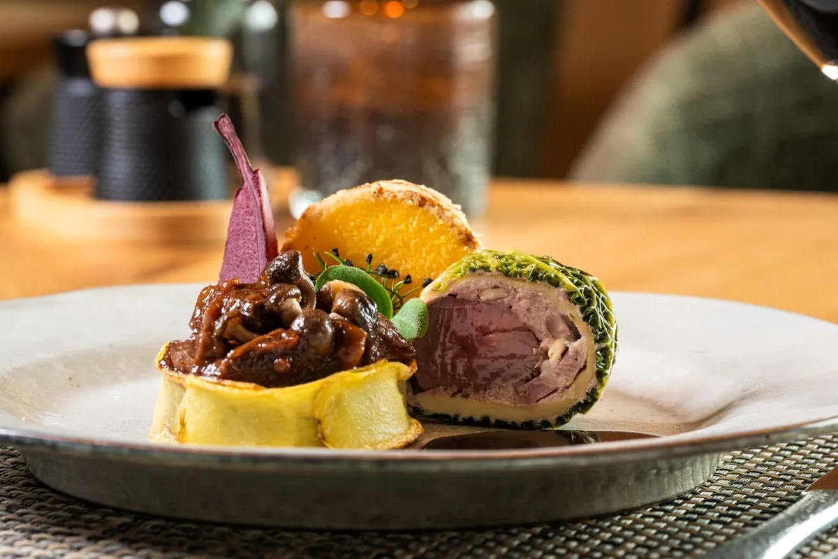 Fleischgericht mit Kräuterkruste, Pilzen und Kartoffelrösti auf Teller