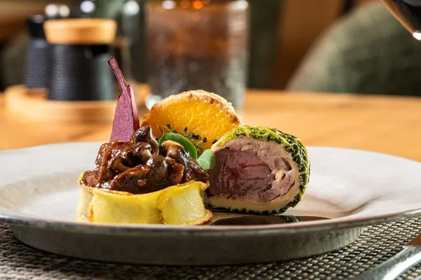 Fleischgericht mit Kräuterkruste, Pilzen und Kartoffelrösti auf Teller