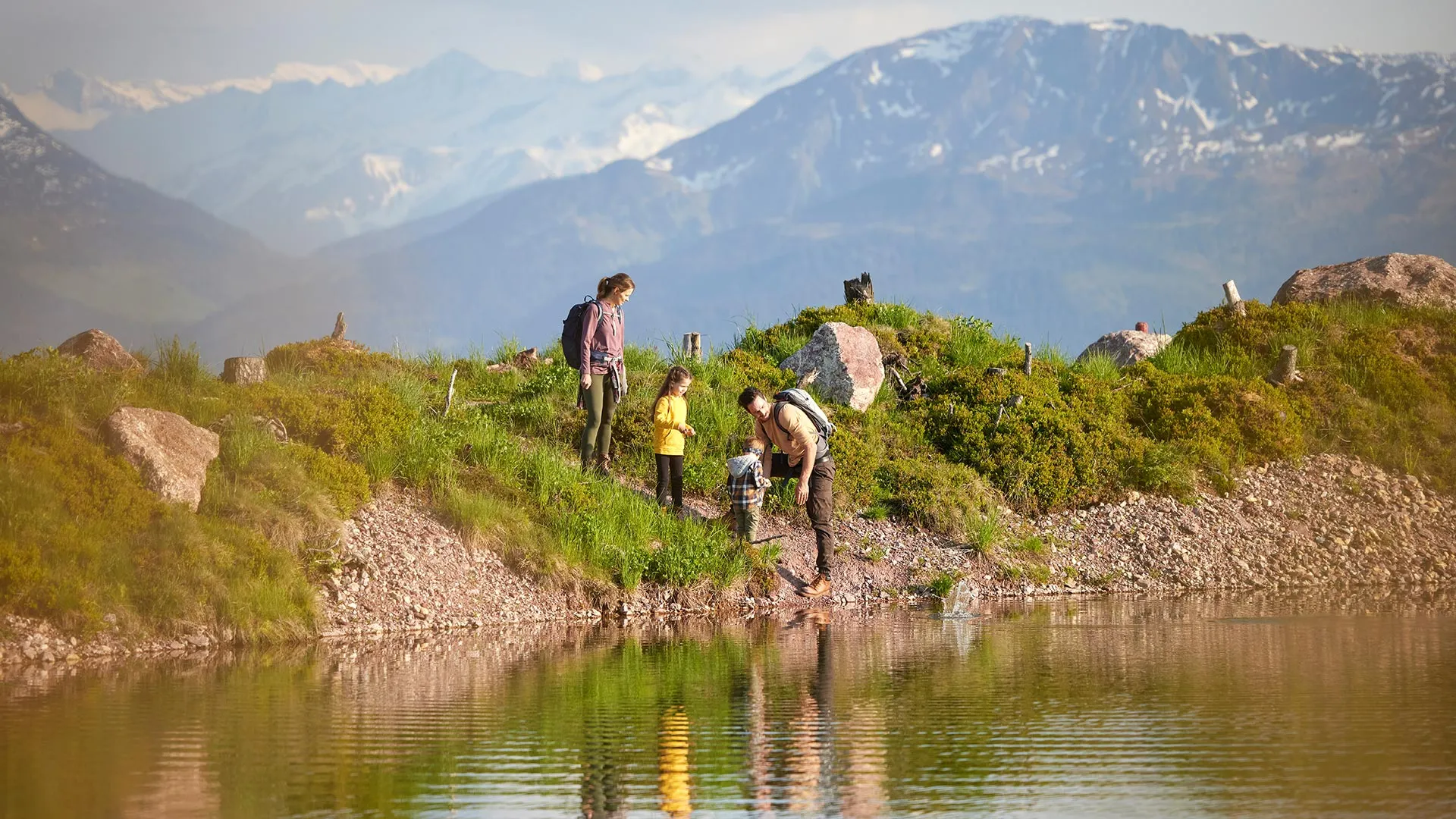 Familie beim Wandern an einem Bergsee mit Blick auf schneebedeckte Gipfel