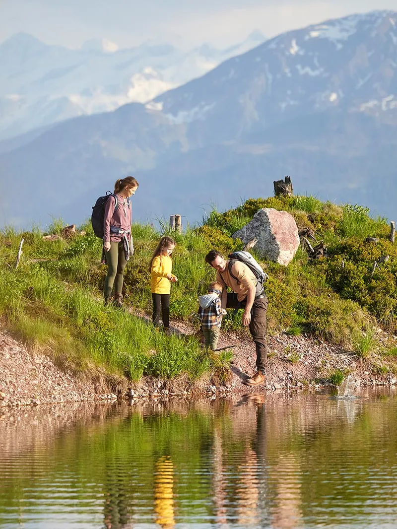 Familie beim Wandern an einem Bergsee mit Blick auf schneebedeckte Gipfel