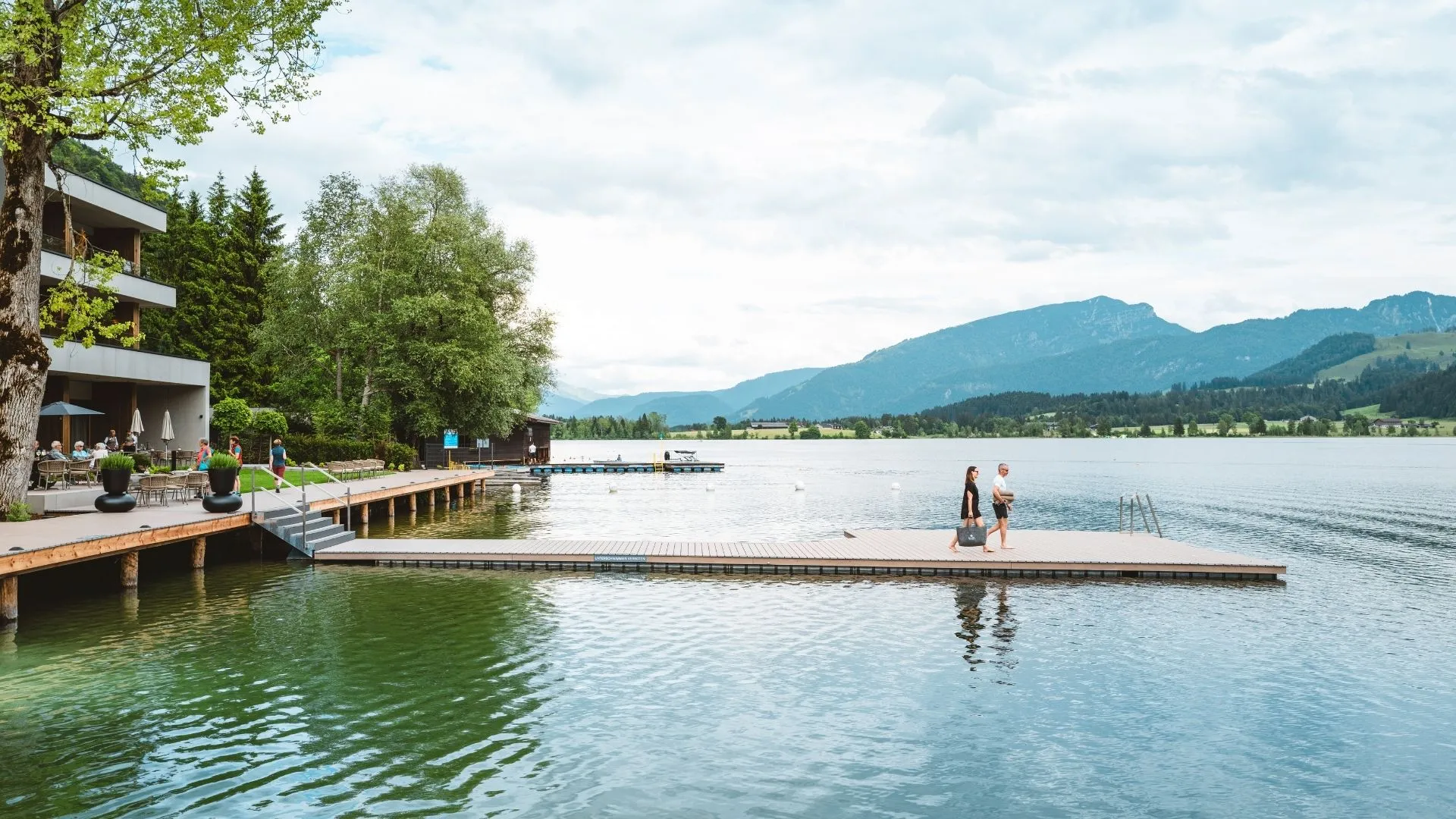 Seesteg am Hotel mit Blick auf Berge und Spaziergänger am Wasser