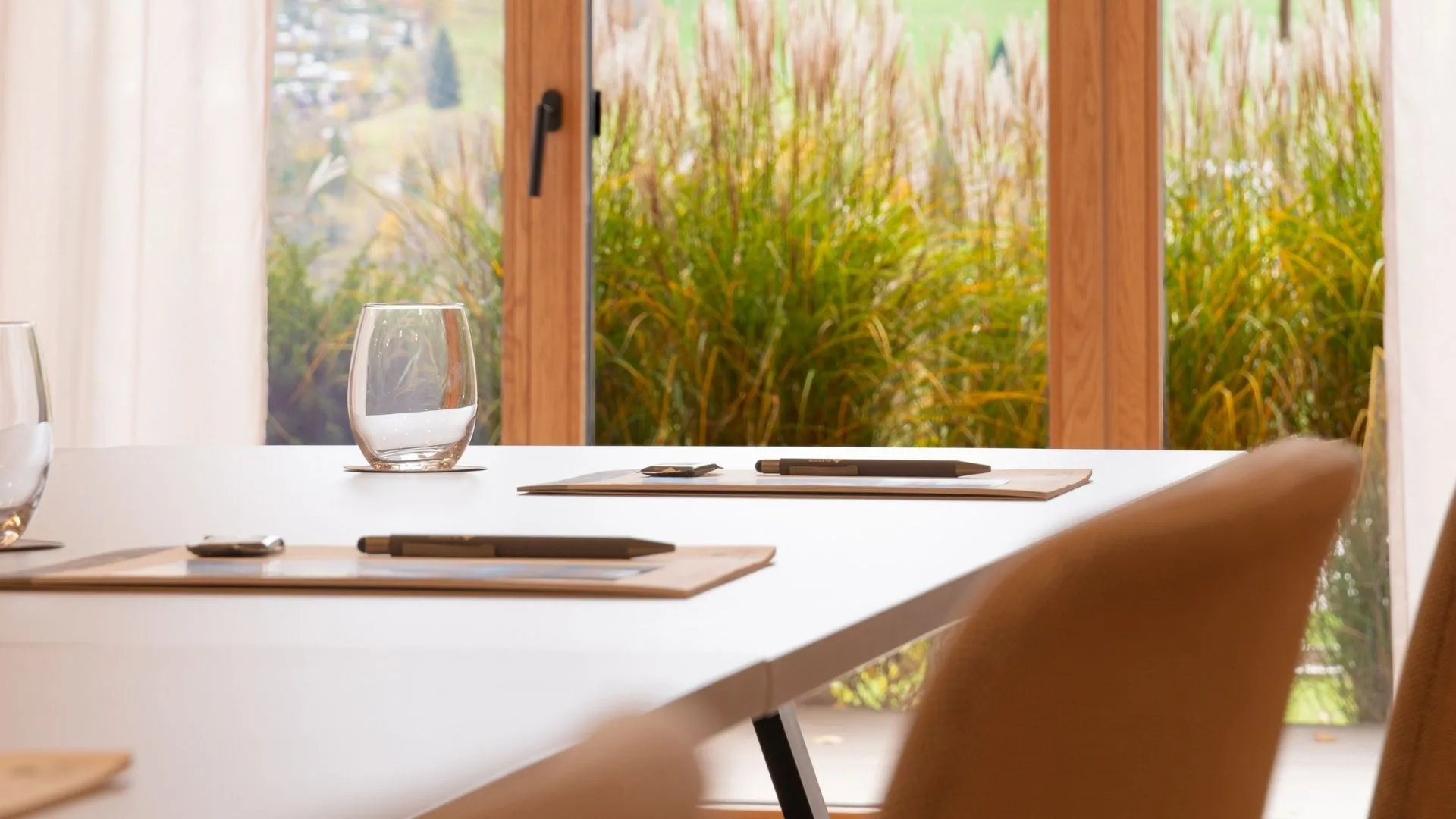 Konferenztisch mit Gläsern und Schreibmappen vor Fenster mit Gartenblick