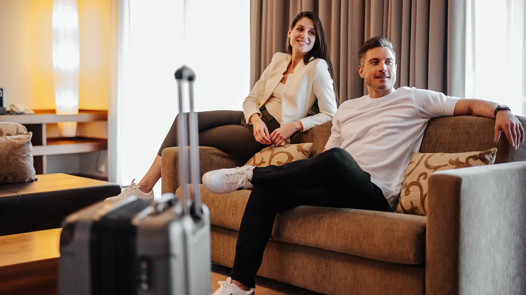 Paar entspannt mit Koffer auf Sofa im Hotelzimmer