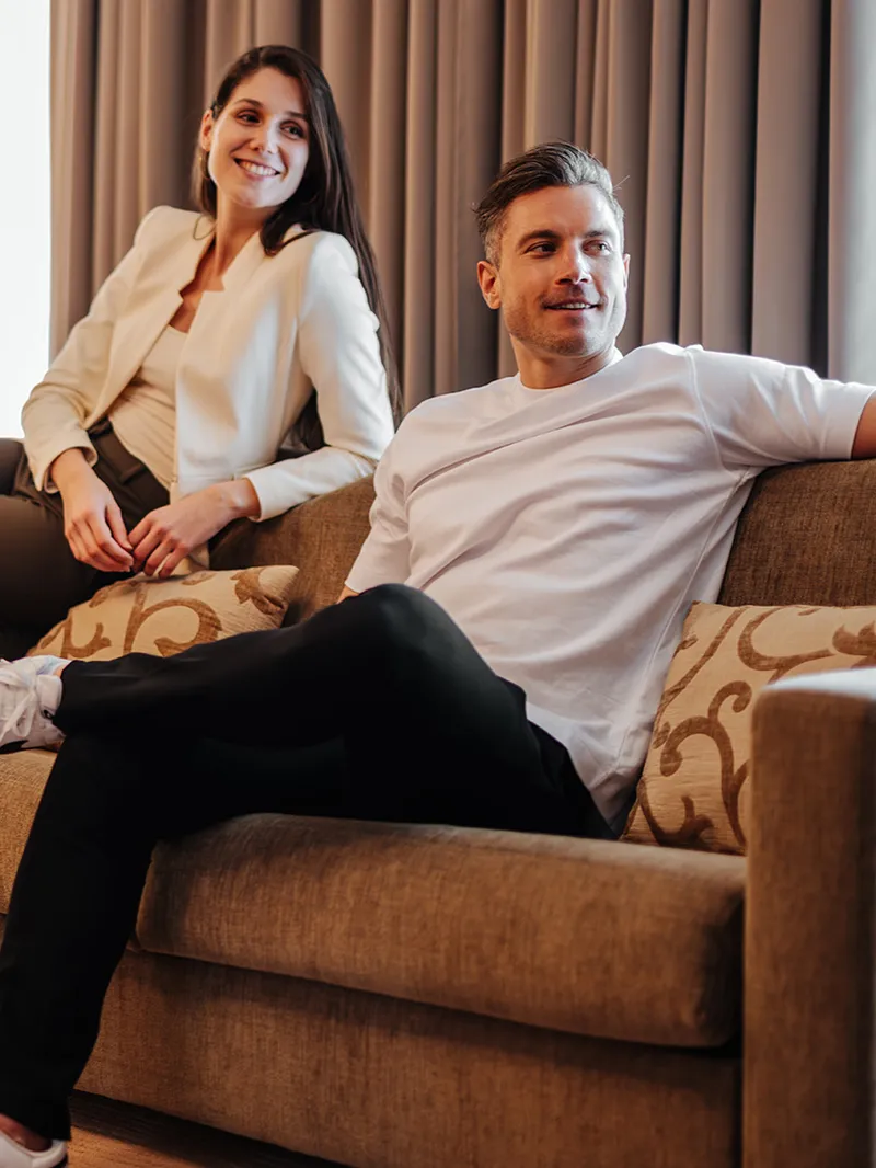 Paar entspannt mit Koffer auf Sofa im Hotelzimmer