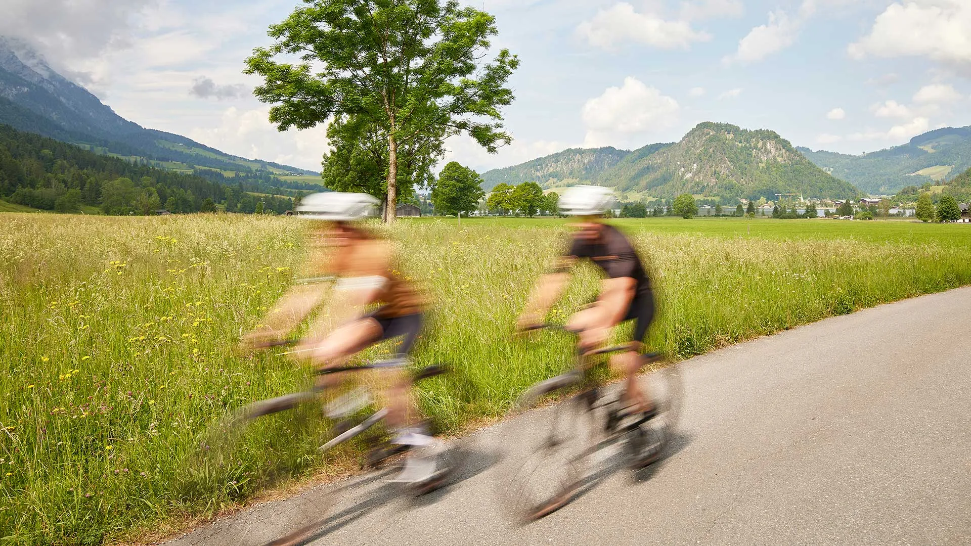 Zwei Rennradfahrer auf Landstraße vor Bergpanorama im Sommer