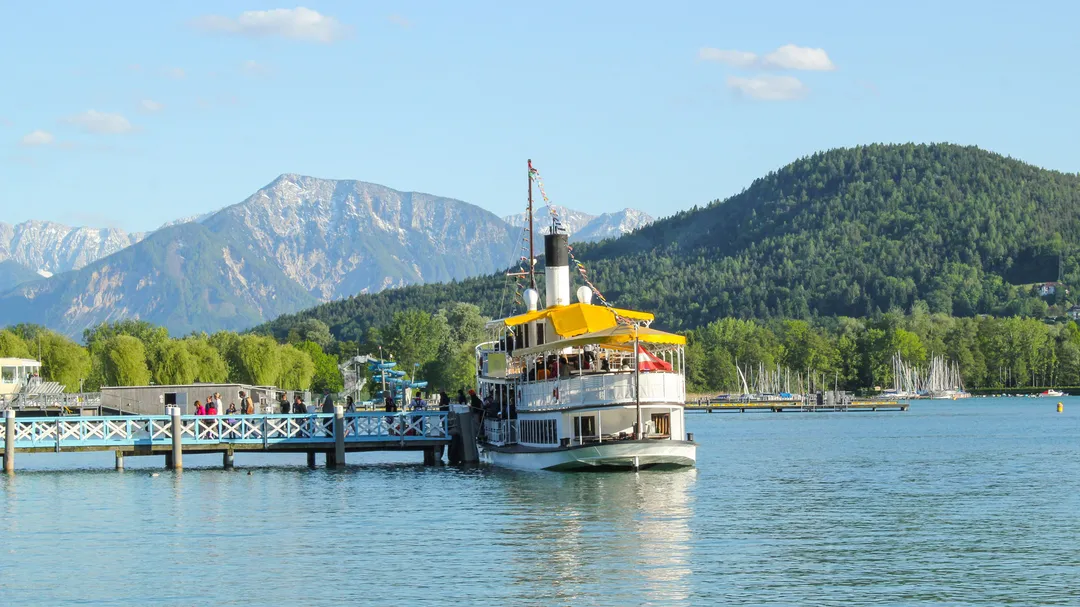 Ausflugsschiff am Steg eines Sees vor Bergkulisse