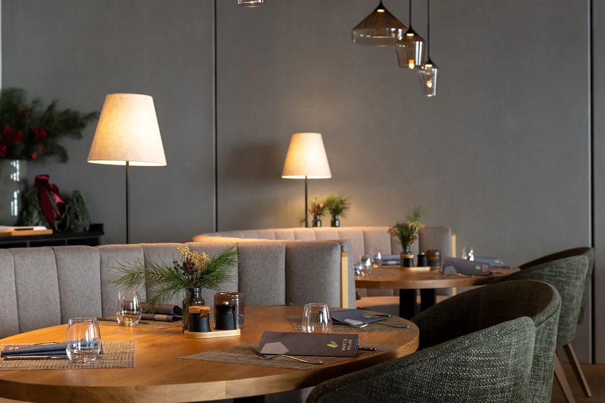Modernes Restaurant mit gemütlichen Sitzecken, Holztischen, warmem Licht und grünen Dekorationen.