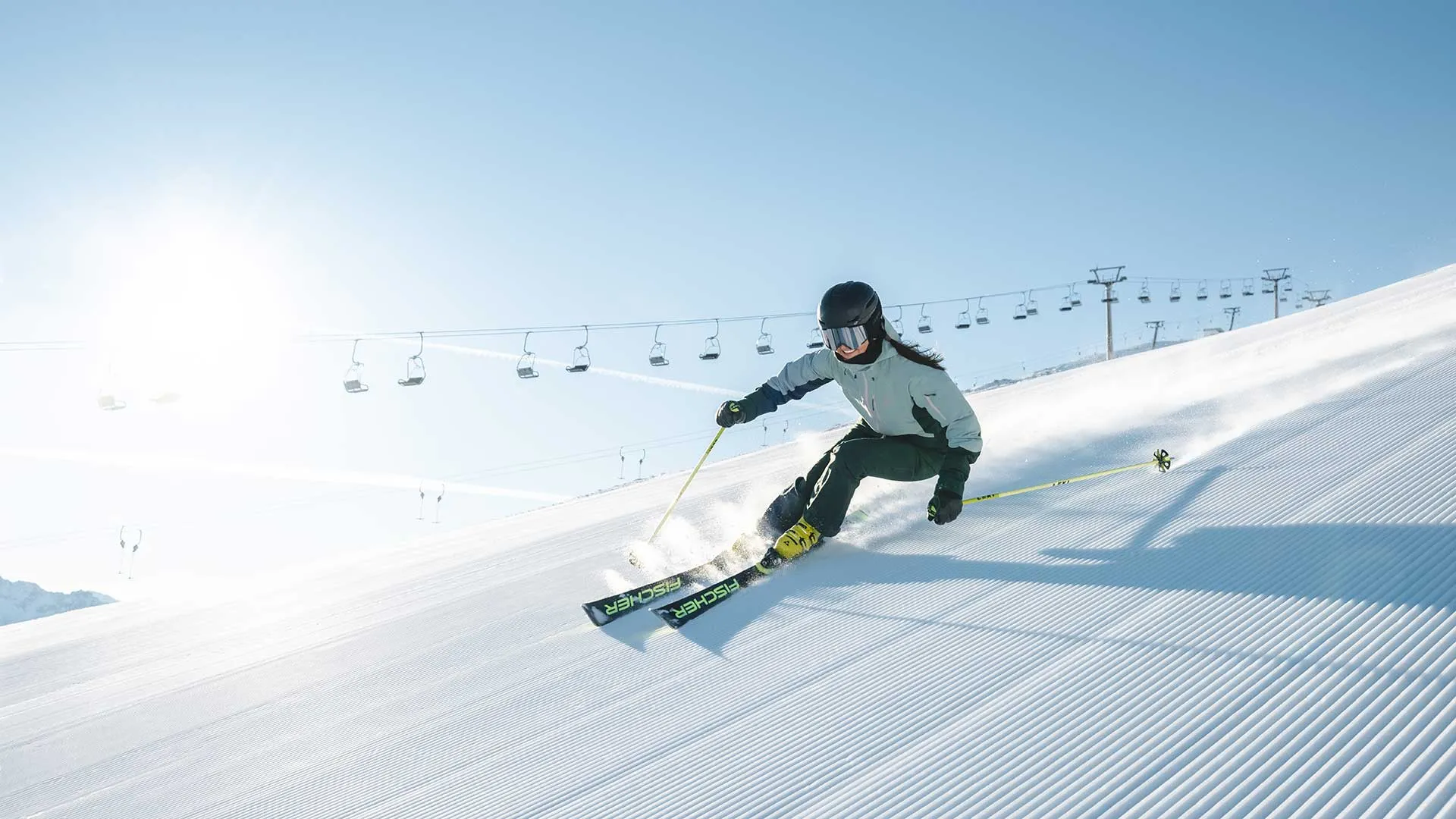 Skifahrerin fährt auf frisch präparierter Piste, im Hintergrund ein Sessellift