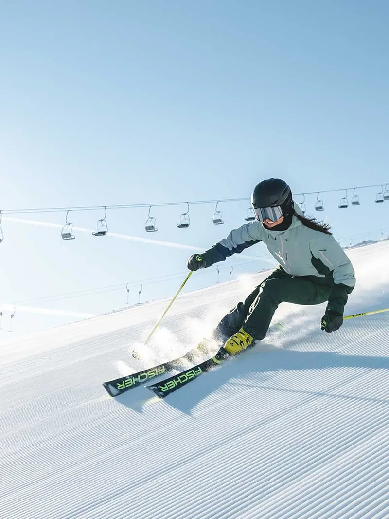 Skifahrerin fährt auf frisch präparierter Piste, im Hintergrund ein Sessellift