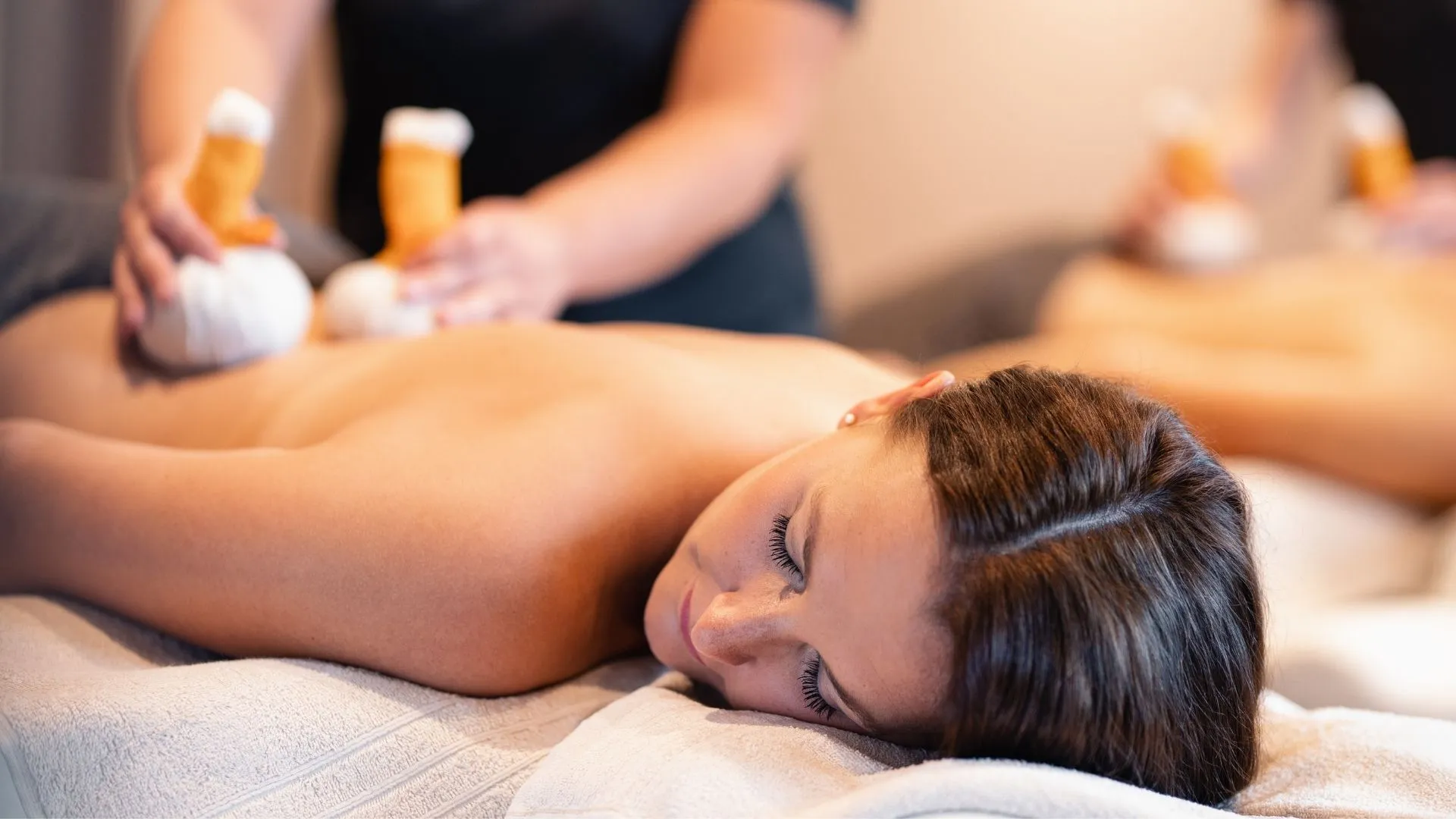 Frau erhält Rückenmassage mit Kräuterstempeln im Spa