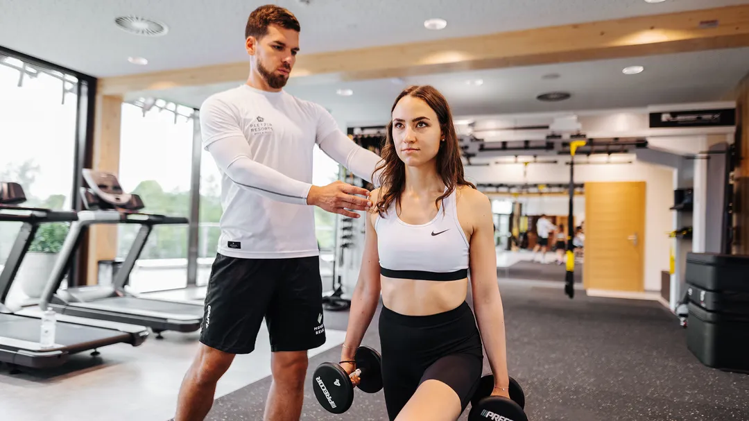 Personal Trainer korrigiert Haltung einer Frau mit Kurzhanteln im Fitnessstudio