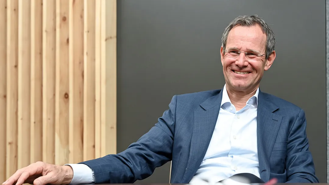 Lächelnder Mann im Anzug sitzt vor Holzwand