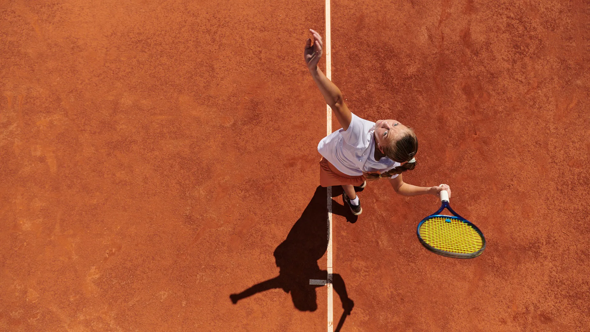 Luftaufnahme einer Tennisspielerin beim Aufschlag auf einem Sandplatz