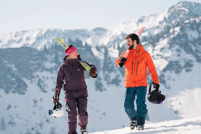 Zwei Skifahrer tragen ihre Skier auf einer schneebedeckten Bergkuppe