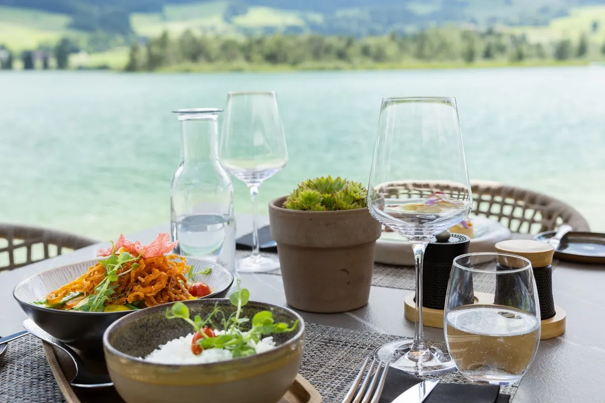 Gedeckter Tisch mit Speisen und Weingläsern vor einem See