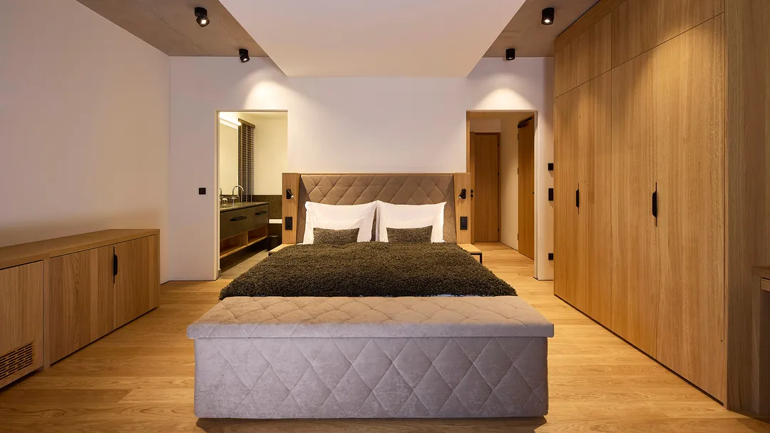 Schlafzimmer mit Doppelbett, Holzschrank und Blick ins Bad