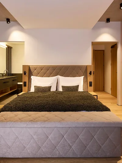 Schlafzimmer mit Doppelbett, Holzschrank und Blick ins Bad