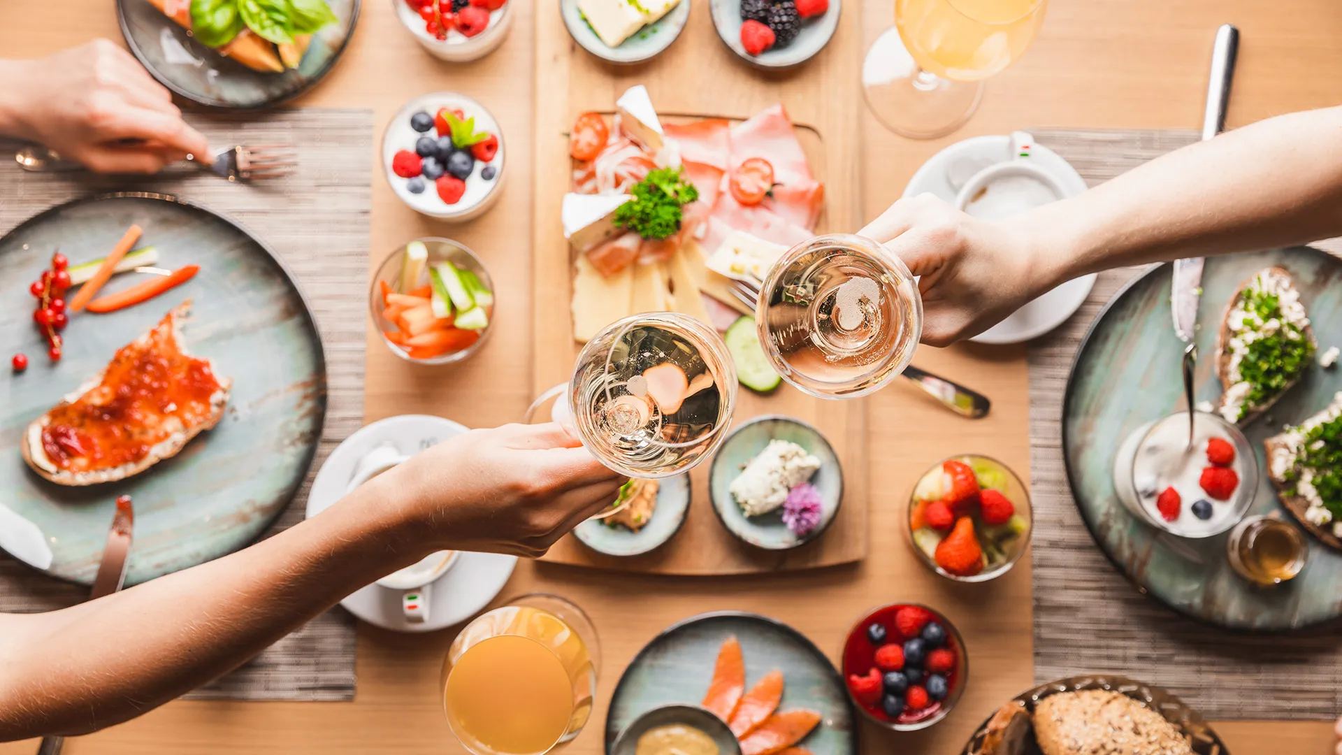 Frühstückstisch von oben mit Obst, Aufschnitt und anstoßenden Sektgläsern