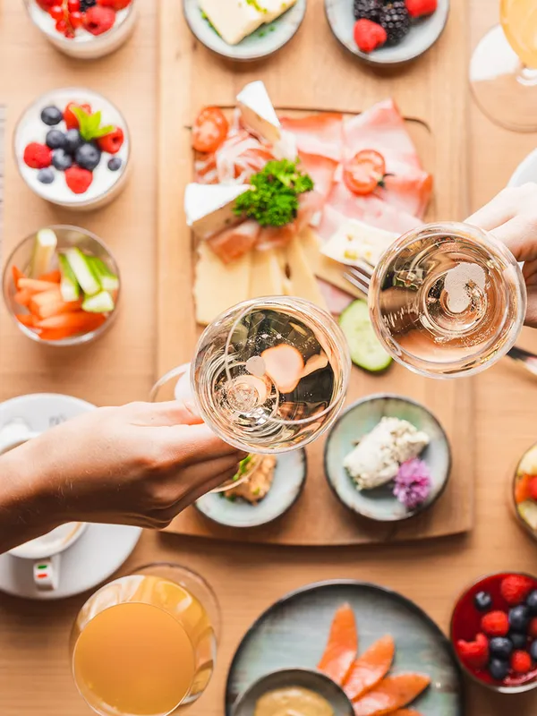 Frühstückstisch von oben mit Obst, Aufschnitt und anstoßenden Sektgläsern