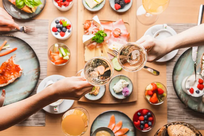 Frühstückstisch von oben mit Obst, Aufschnitt und anstoßenden Sektgläsern