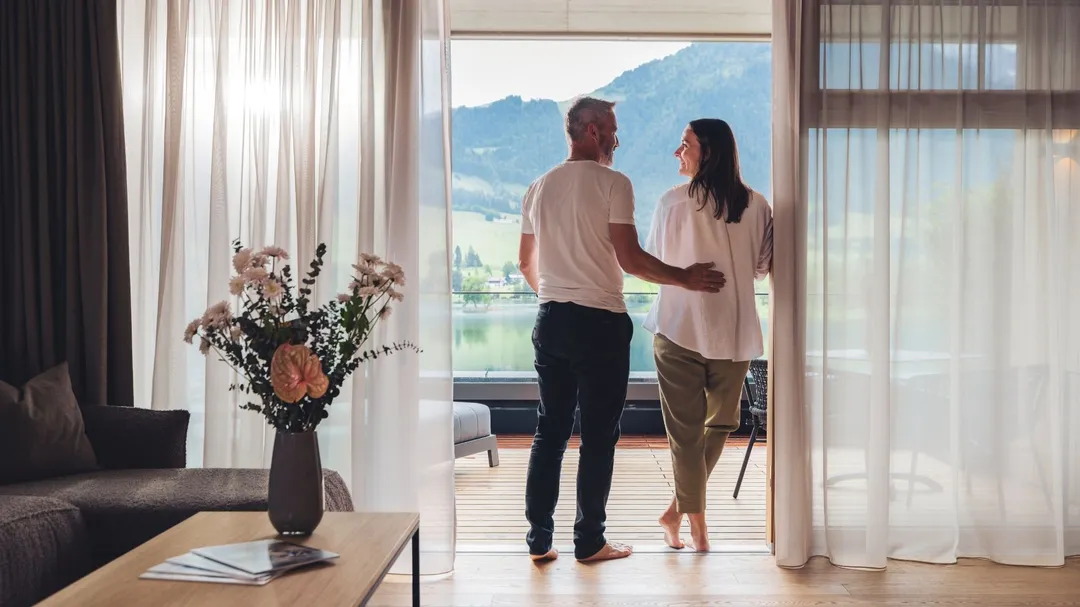 Paar blickt vom Balkon eines Hotelzimmers auf See und Berge
