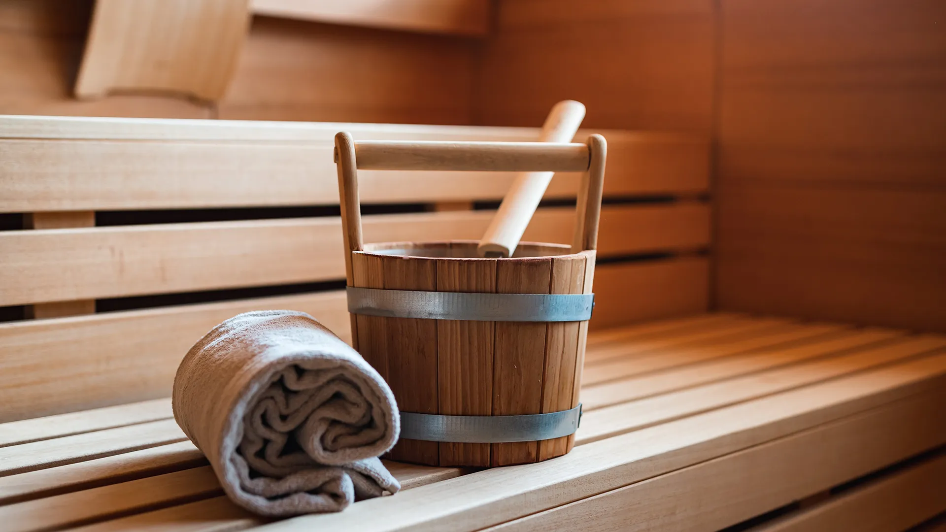 Saunaeimer mit Schöpfkelle und Handtuch auf Holzbank in der Sauna