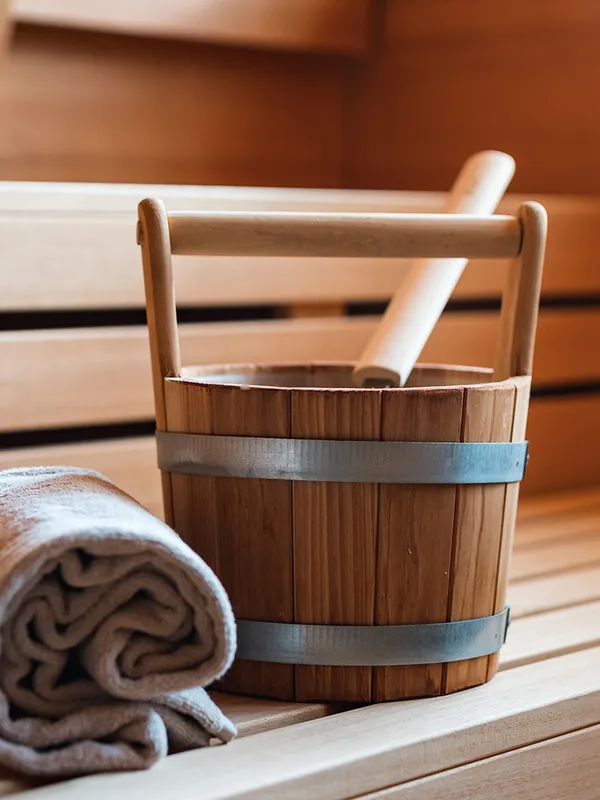 Saunaeimer mit Schöpfkelle und Handtuch auf Holzbank in der Sauna
