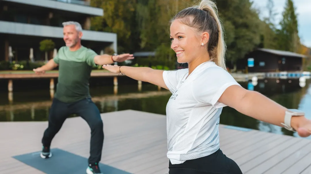 Frau und Mann machen Yoga auf einem Steg am See