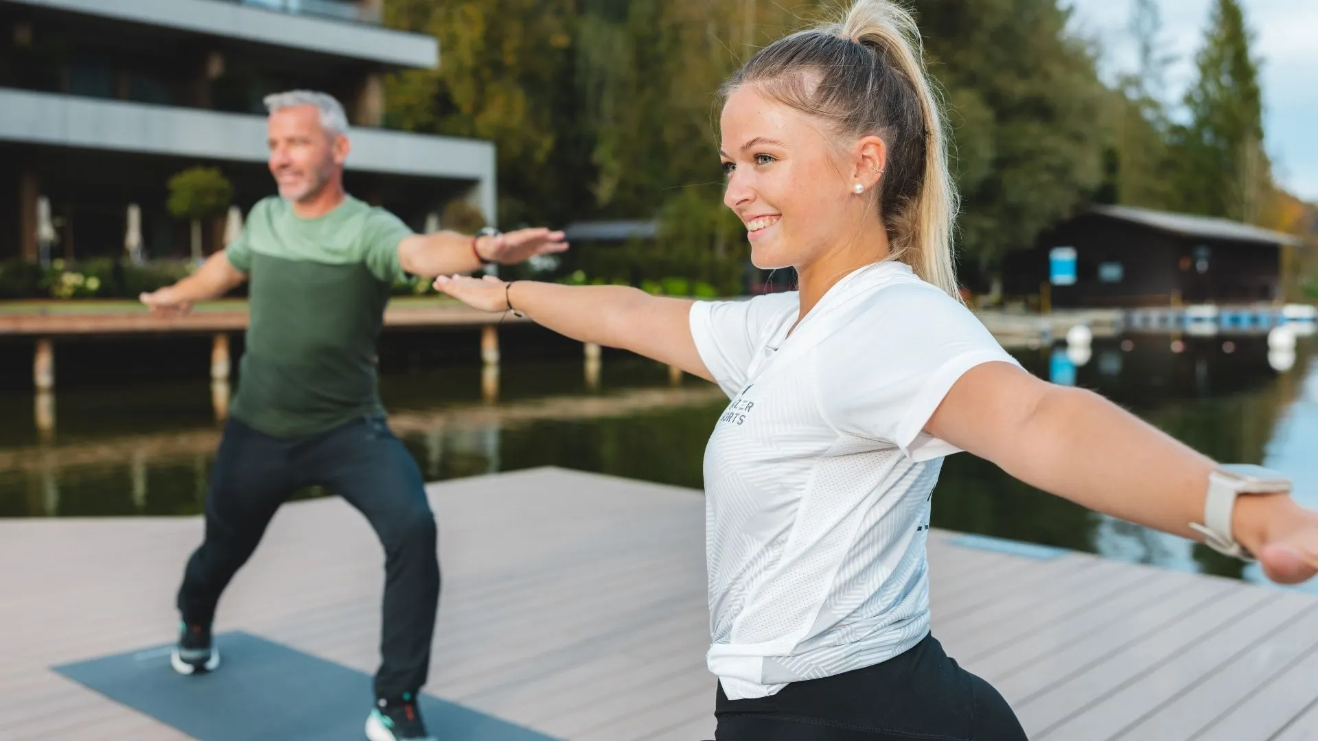 Frau und Mann machen Yoga auf einem Steg am See