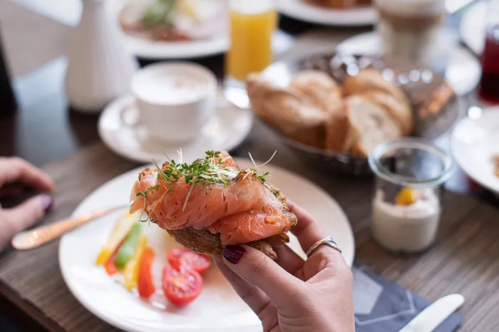 Hand hält Brot mit Lachs beim Frühstücksbuffet mit Brot, Kaffee und Saft