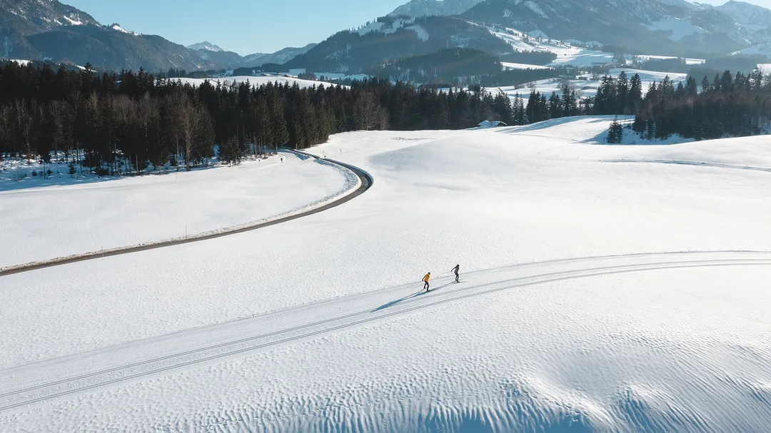 Zwei Langläufer auf präparierter Loipe in verschneiter Berglandschaft