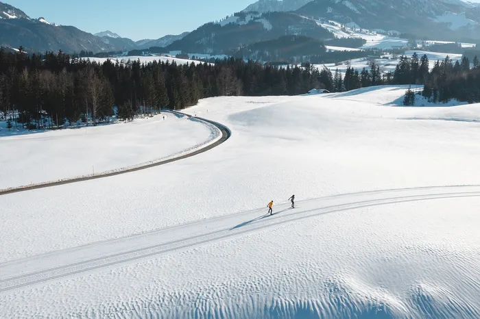 Zwei Langläufer auf präparierter Loipe in verschneiter Berglandschaft