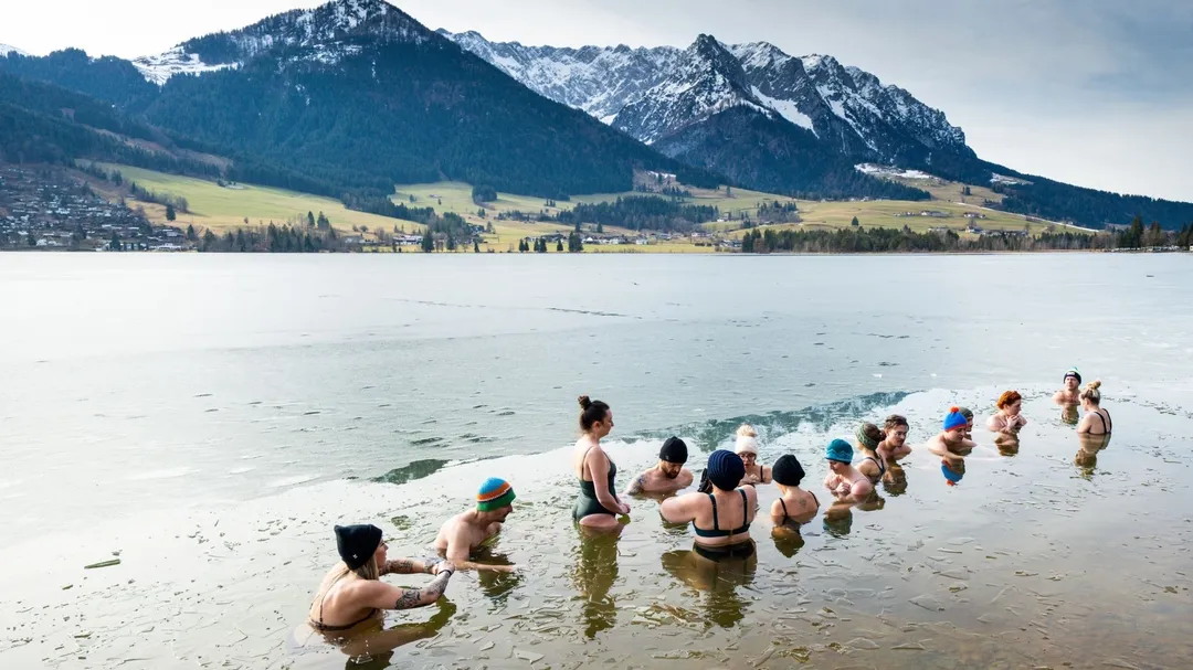 Gruppe beim Eisbaden im See vor schneebedeckter Bergkette