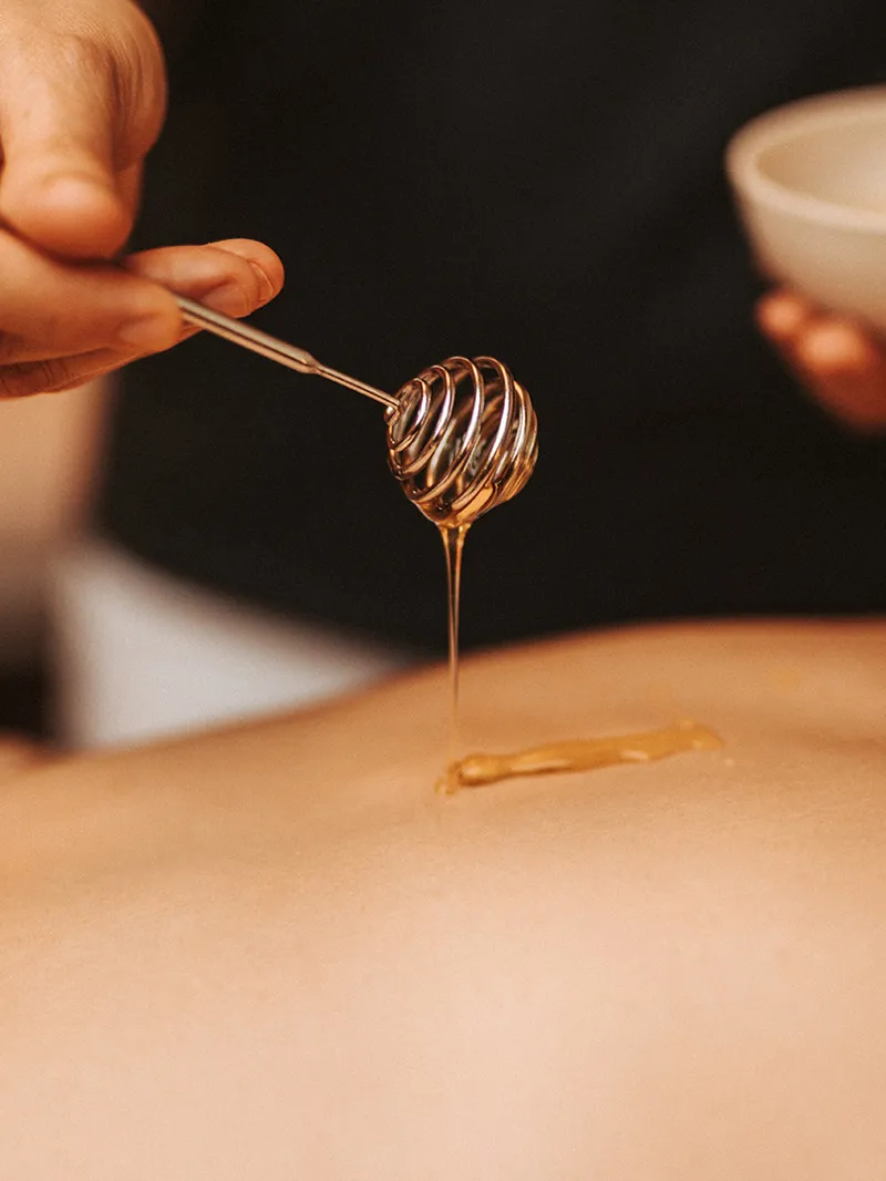 Honig wird mit einem Honigträufler auf den Rücken für eine Massage aufgetragen