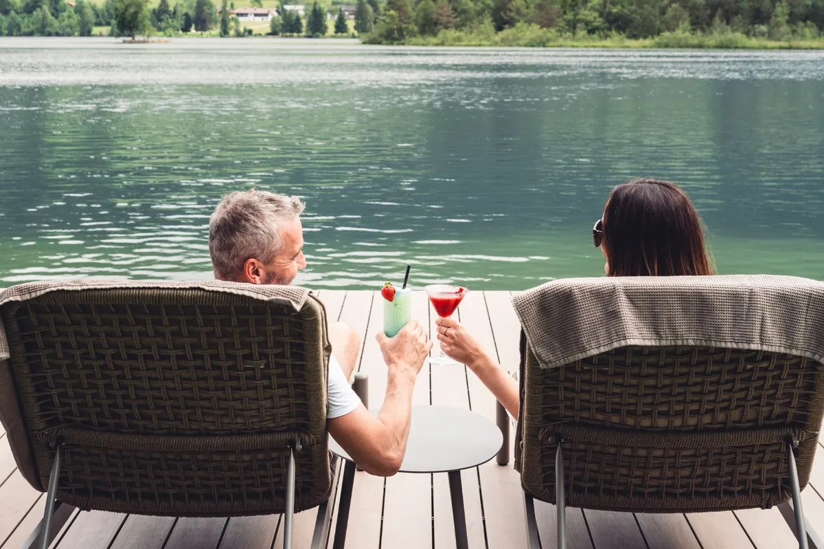 Paar sitzt mit Cocktails auf Liegestühlen am See
