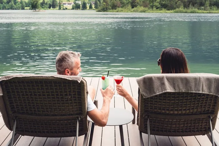 Paar sitzt mit Cocktails auf Liegestühlen am See