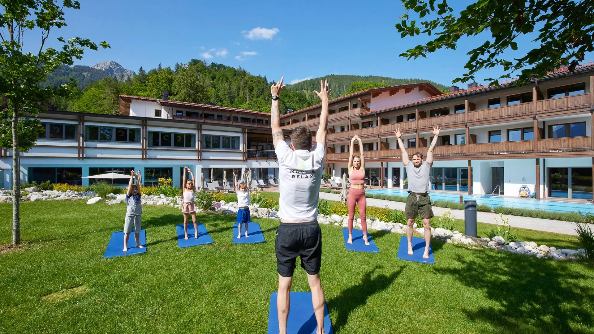 Yogastunde im Garten vor dem Hotel mit Erwachsenen und Kindern auf Matten
