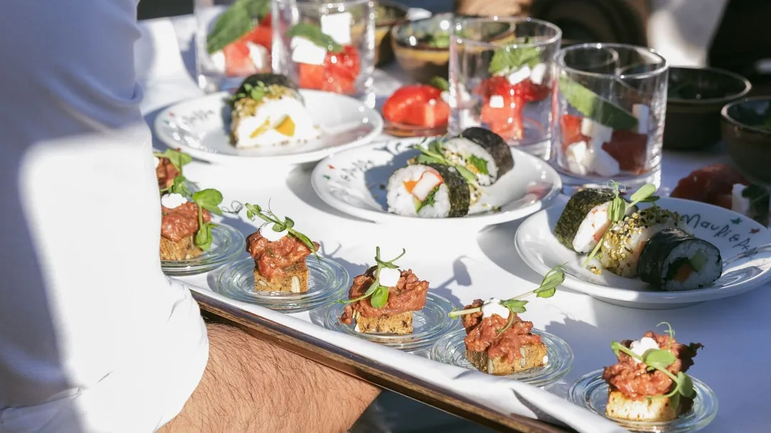 Kellner serviert Tablett mit Sushi, Tatar-Häppchen und Gläsern mit Wassermelonensalat
