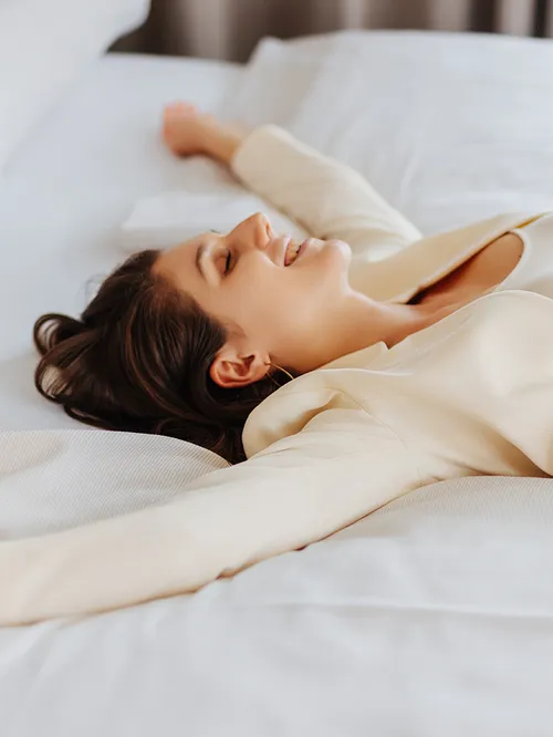 Frau entspannt sich lächelnd auf einem weißen Hotelbett