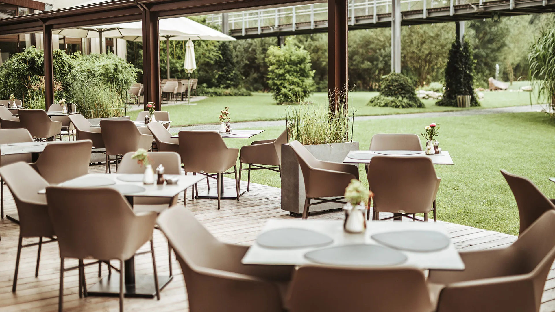 Überdachte Restaurantterrasse mit gedeckten Tischen und Gartenblick