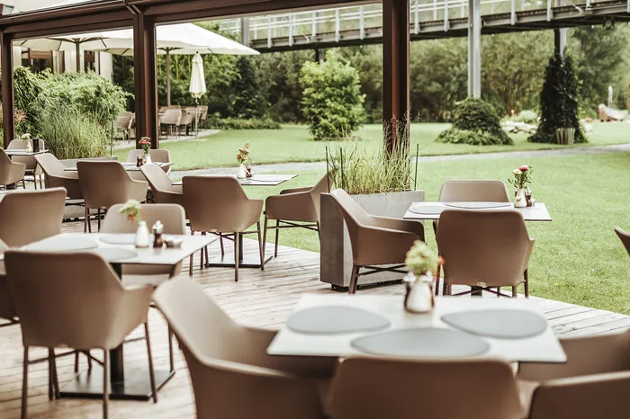 Überdachte Restaurantterrasse mit gedeckten Tischen und Gartenblick