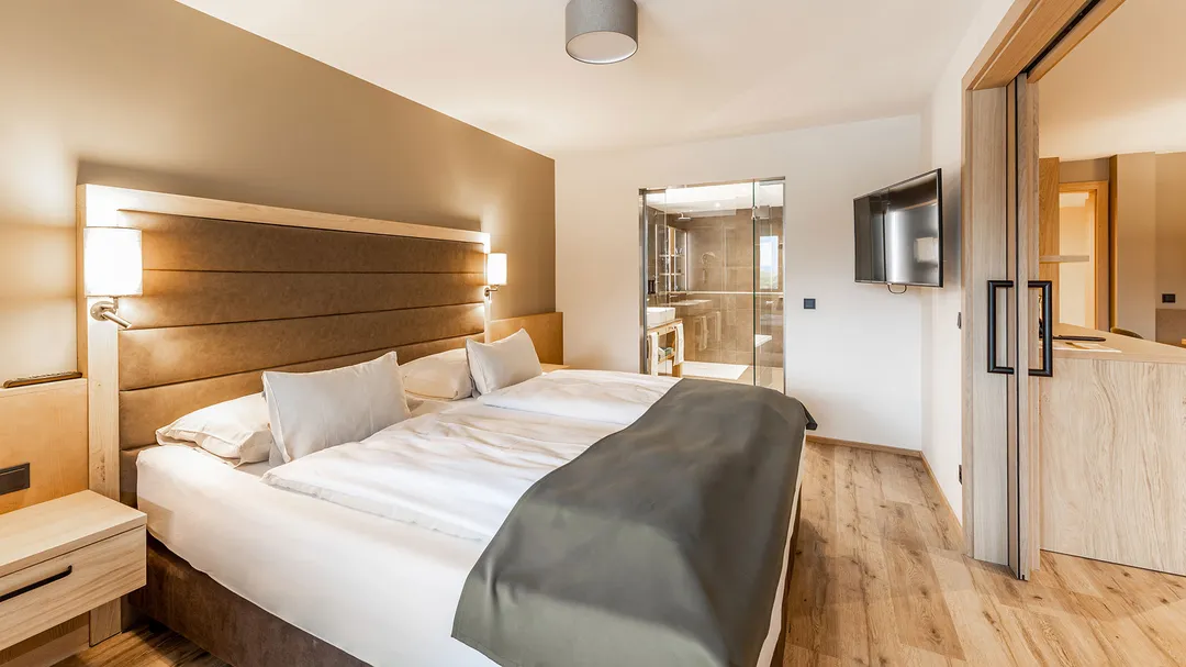 Hotelzimmer mit Doppelbett, Holzboden und Blick ins Bad mit Glaswand