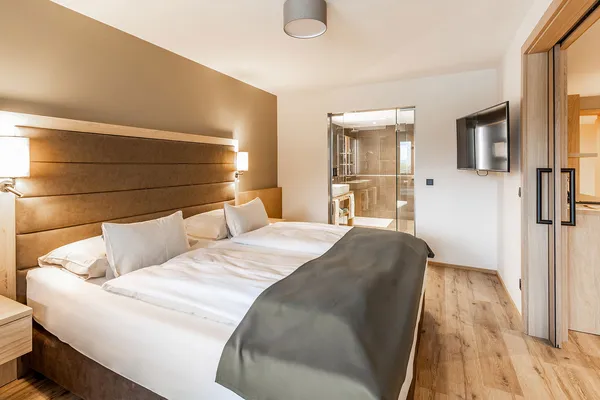 Hotelzimmer mit Doppelbett, Holzboden und Blick ins Bad mit Glaswand