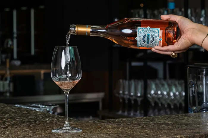 Rosé Wein wird an der Bar in ein Glas eingeschenkt