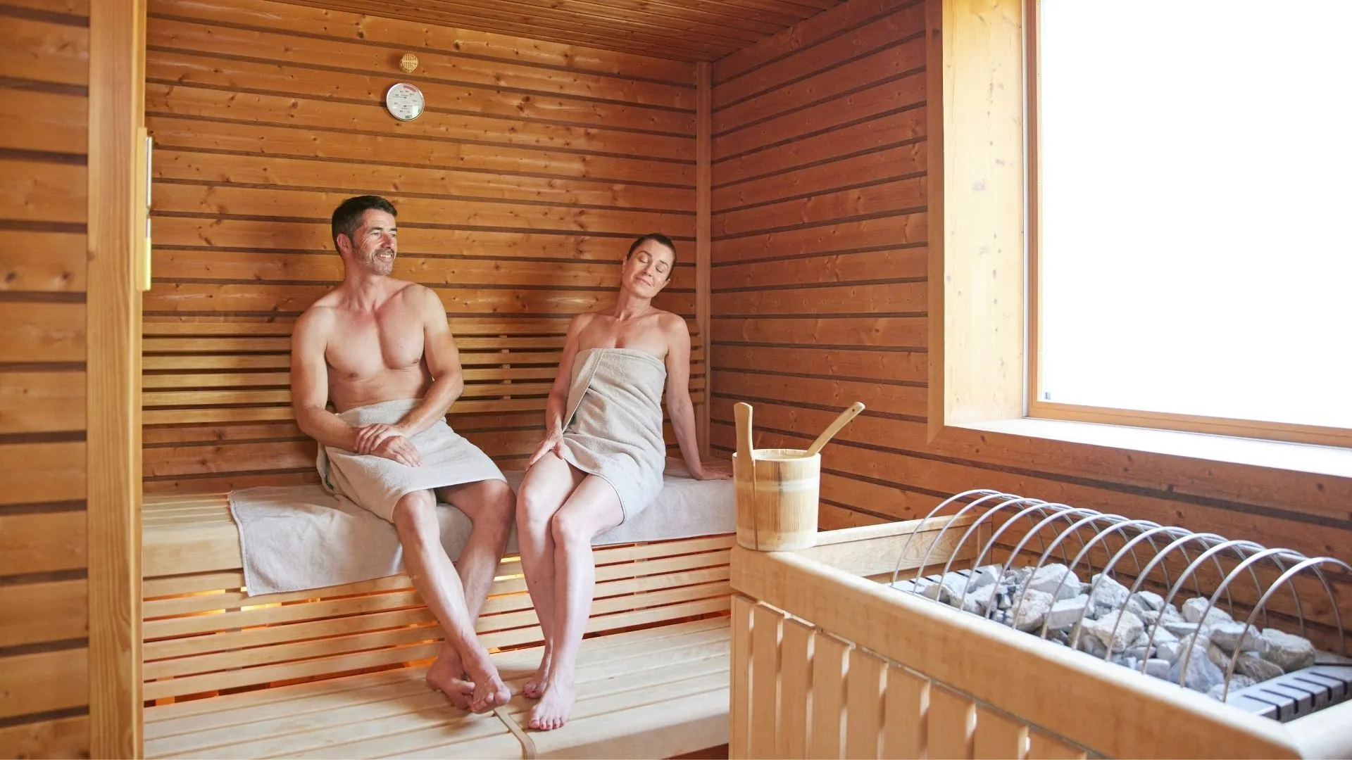 Mann und Frau entspannen in Holzsauna mit Saunaofen