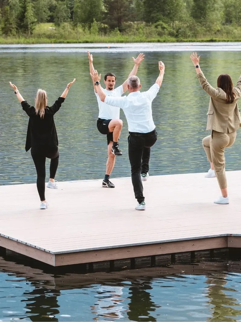 Gruppe macht Yoga-Baumhaltung auf Holzsteg am See
