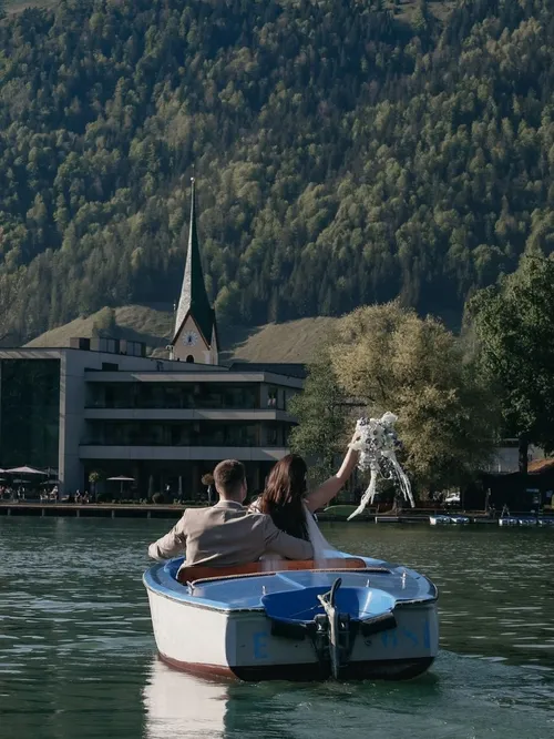 Brautpaar im Ruderboot auf einem See vor Hotel und Bergkulisse
