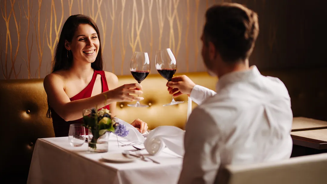 Paar stößt mit Rotwein an einem festlich gedeckten Restauranttisch an